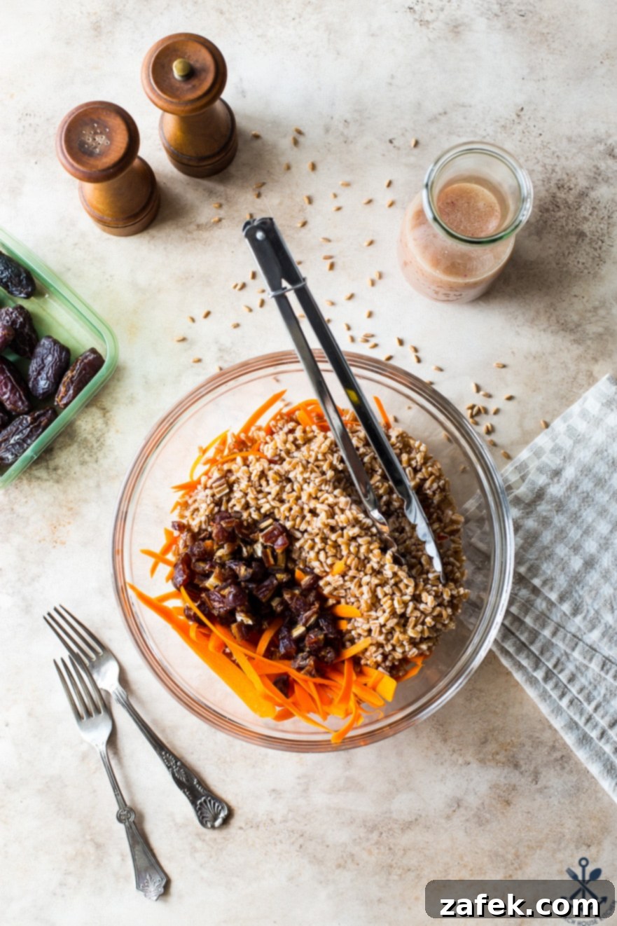 Farro and Carrot Salad with Maple-Date Vinaigrette 4 Close-up overhead photo of a glass bowl filled with the vibrant ingredients of the salad: thinly shredded carrots, plump Medjool dates, and nutty farro, ready to be tossed.
