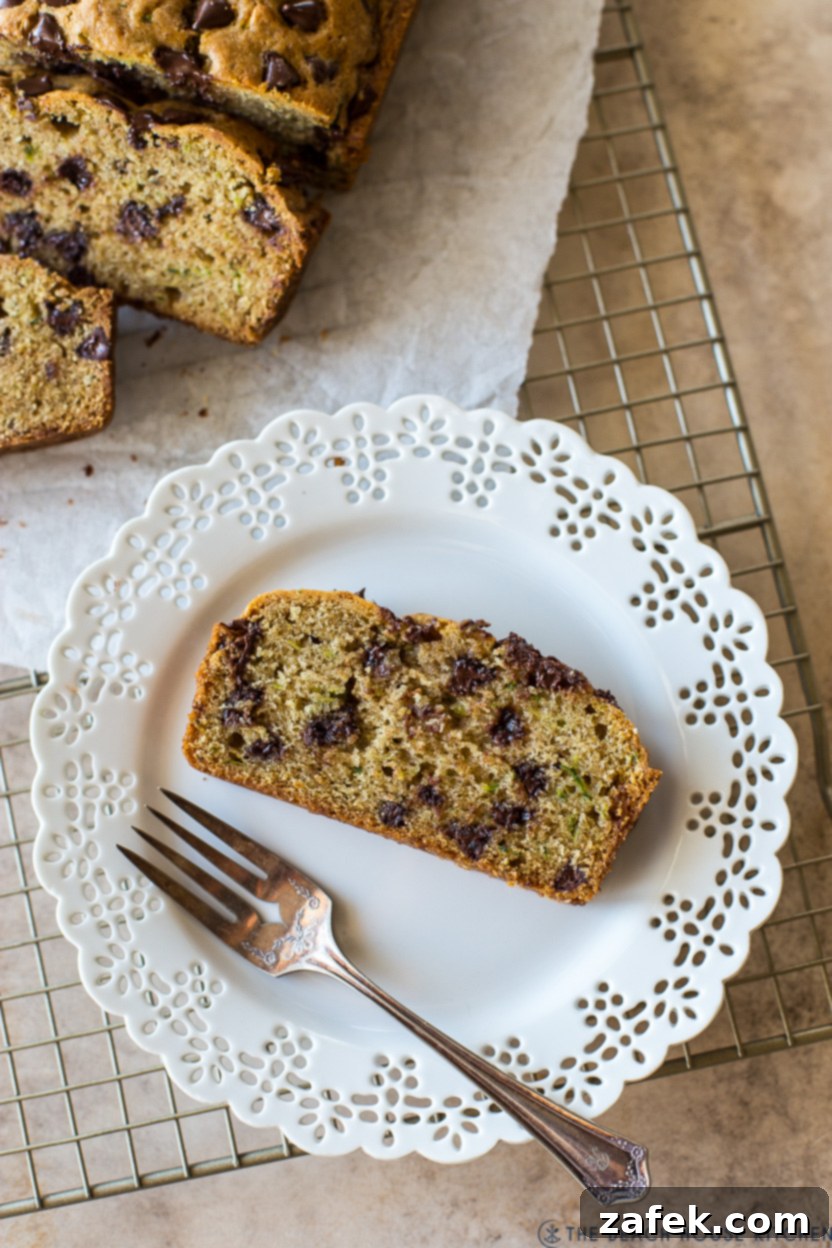Decadent Chocolate Chip Zucchini Loaf 4 Overhead photo of a perfectly sliced piece of chocolate chip zucchini bread on a white plate with a fork.