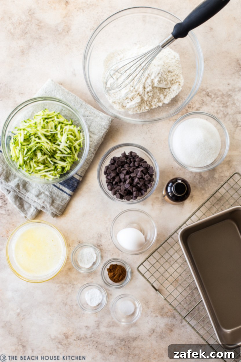 Decadent Chocolate Chip Zucchini Loaf 6 Overhead photo of various ingredients for chocolate chip zucchini bread laid out, including flour, sugar, eggs, butter, chocolate chips, and shredded zucchini.