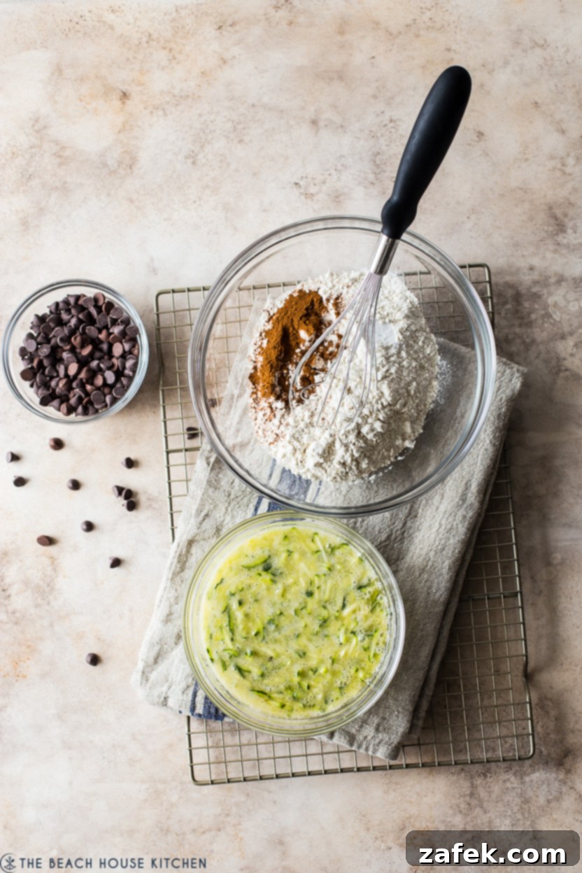 Decadent Chocolate Chip Zucchini Loaf 7 Overhead photo of three bowls: one with dry ingredients, one with wet zucchini mixture, and a small bowl of chocolate chips.
