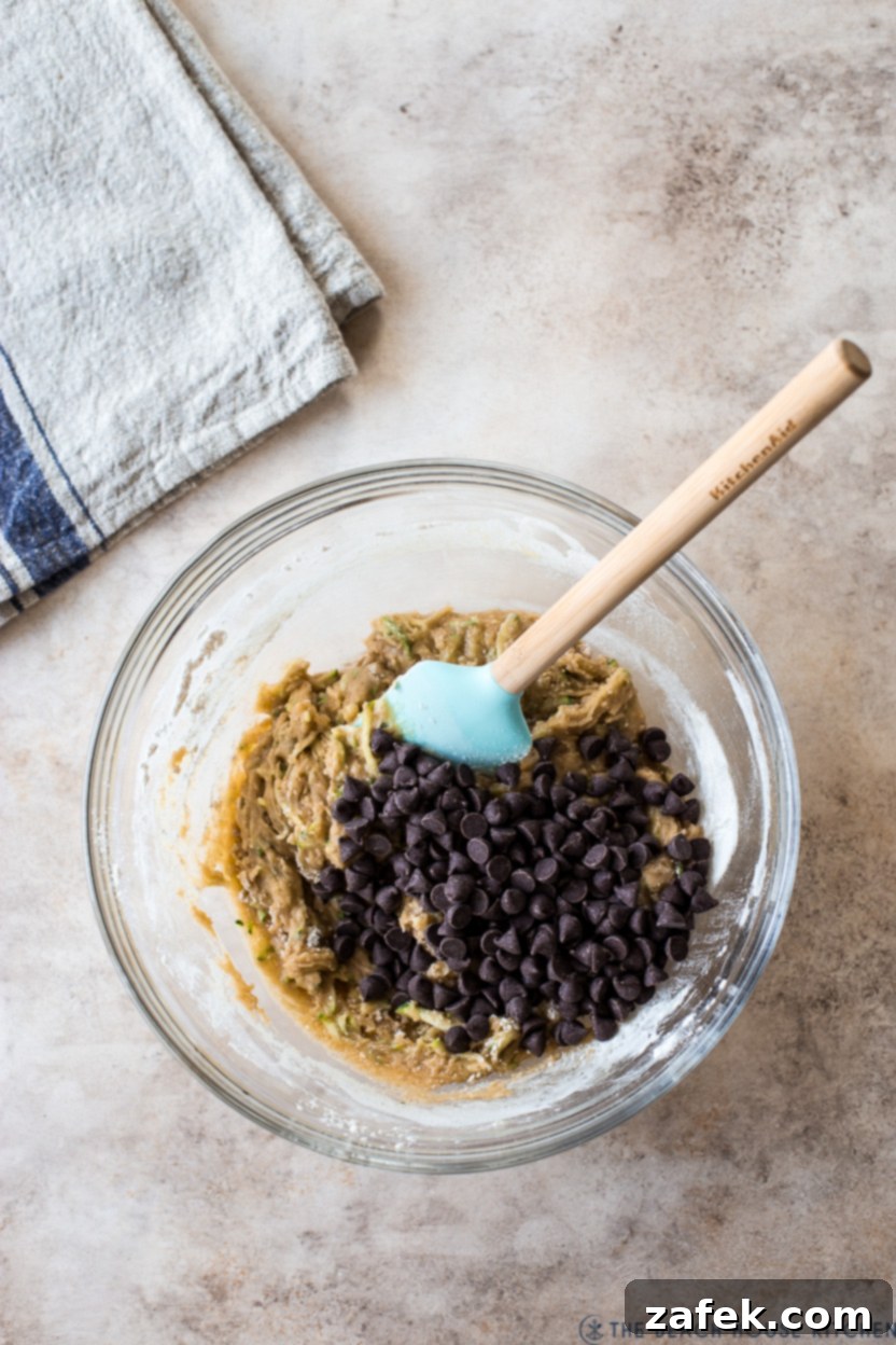 Decadent Chocolate Chip Zucchini Loaf 8 Overhead photo of a bowl filled with zucchini bread batter, topped with a sprinkle of chocolate chips.