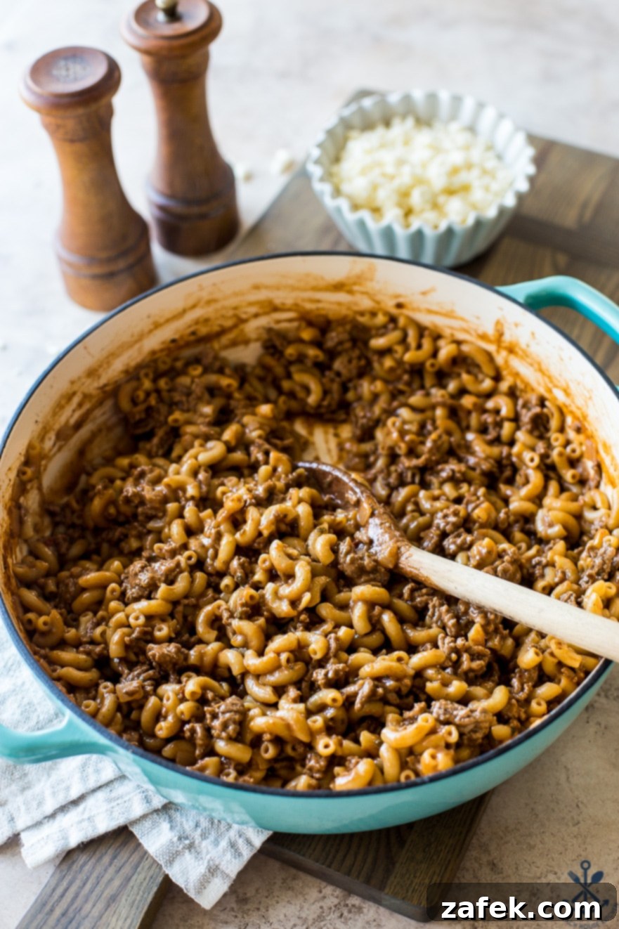 Homemade Greek Beef and Orzo Skillet 5 A skillet of hamurger and pasta with wooden salt and pepper shakers and a small bowl of feta crumbles in the background