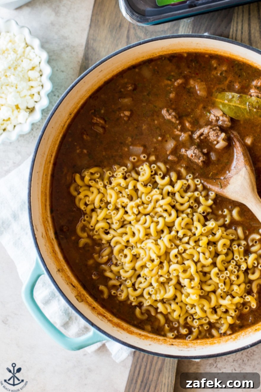 Homemade Greek Beef and Orzo Skillet 8 Up close overhead photo of a skillet filled with broth and dried pasta