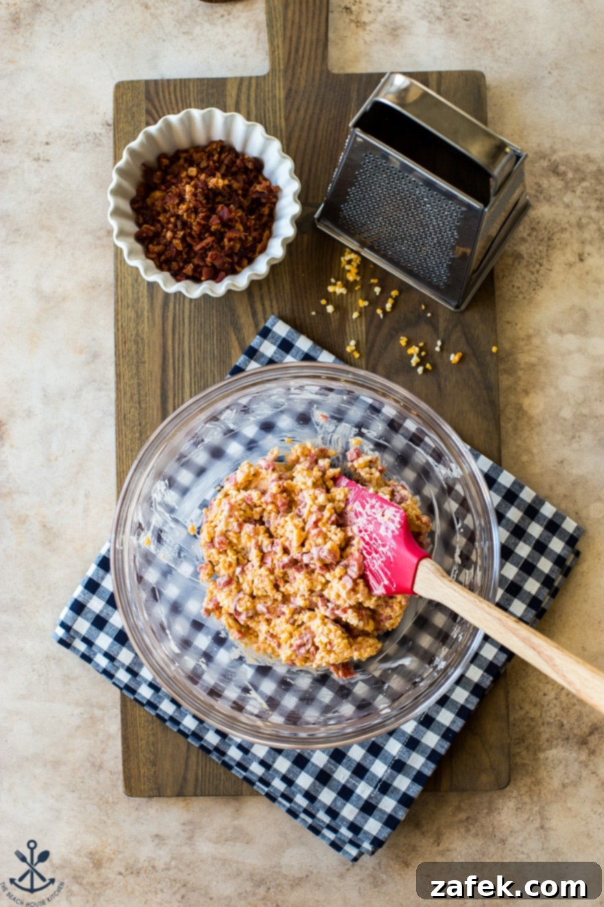 Bacon Pimento Cheese Poppers 7 Overhead photo of a glass bowl filled with piemnto cheese on a wooden board with a small bowl of bacon bits and a cheese grater off to the side