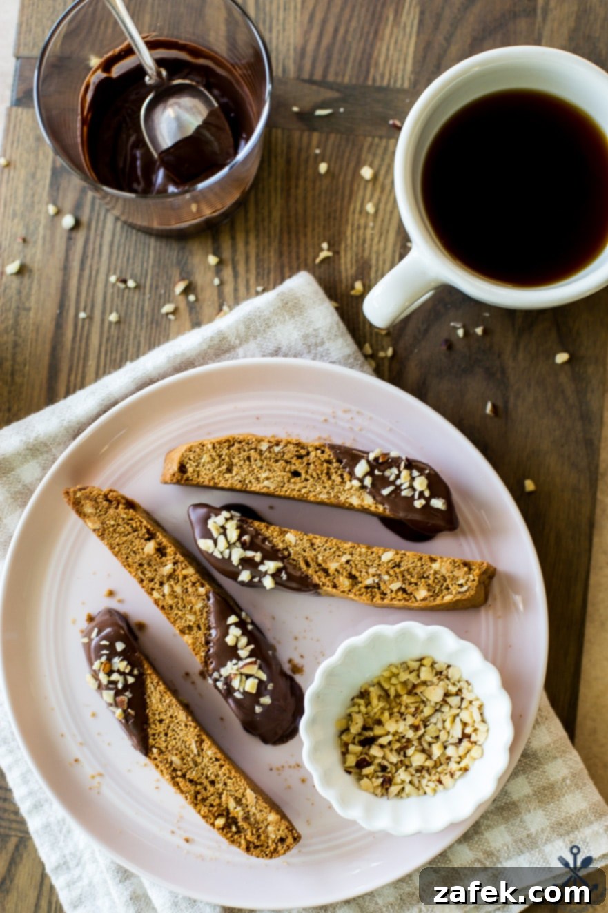 Four slices of Chocolate Dipped Hazelnut Espresso Biscotti elegantly arranged on a plate, alongside a small bowl of whole hazelnuts and a steaming cup of coffee