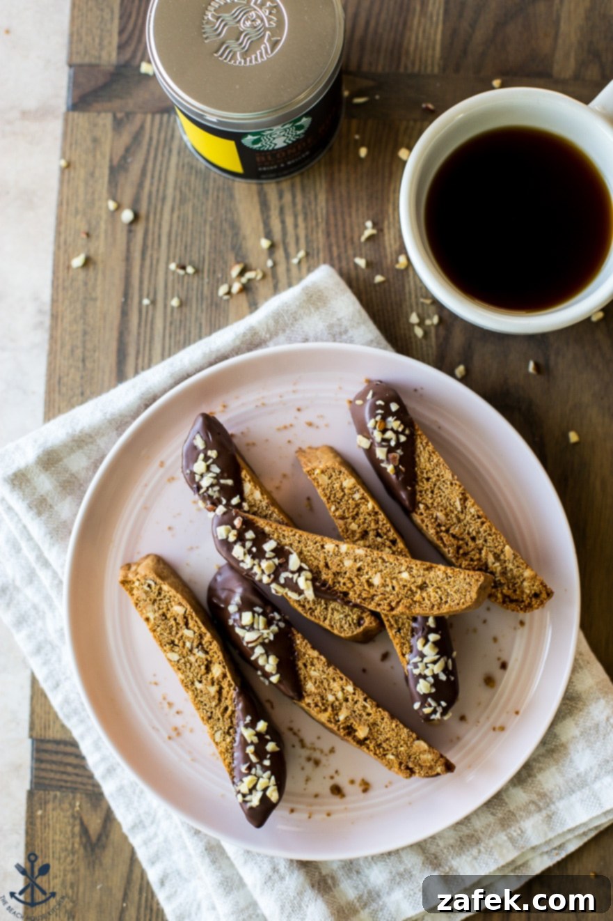 A charming close-up of a pink plate laden with finished Chocolate Dipped Hazelnut Espresso Biscotti, accompanied by a cup of coffee