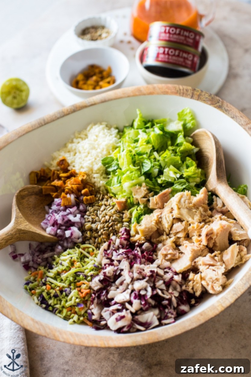 A rustic wooden bowl filled with Thai Chili Mango Tuna Chopped Salad, accompanied by wooden serving utensils.