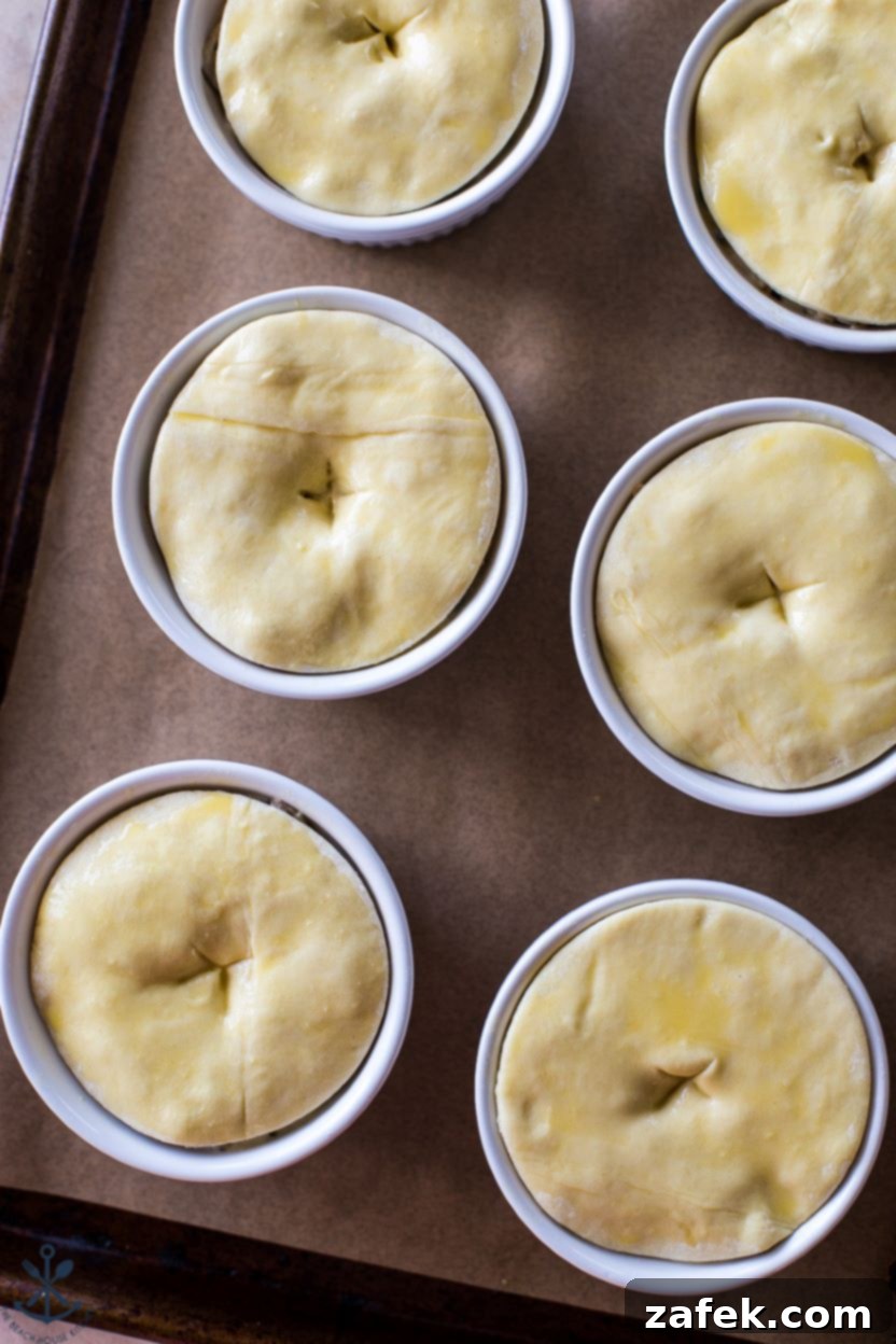 Flaky Puff Chicken Pot Pie 8 Six individual chicken pot pies, expertly topped with golden, flaky puff pastry and arranged on a baking sheet, ready for the oven. Each pastry top has small slits for steam release, promising a perfectly baked result.