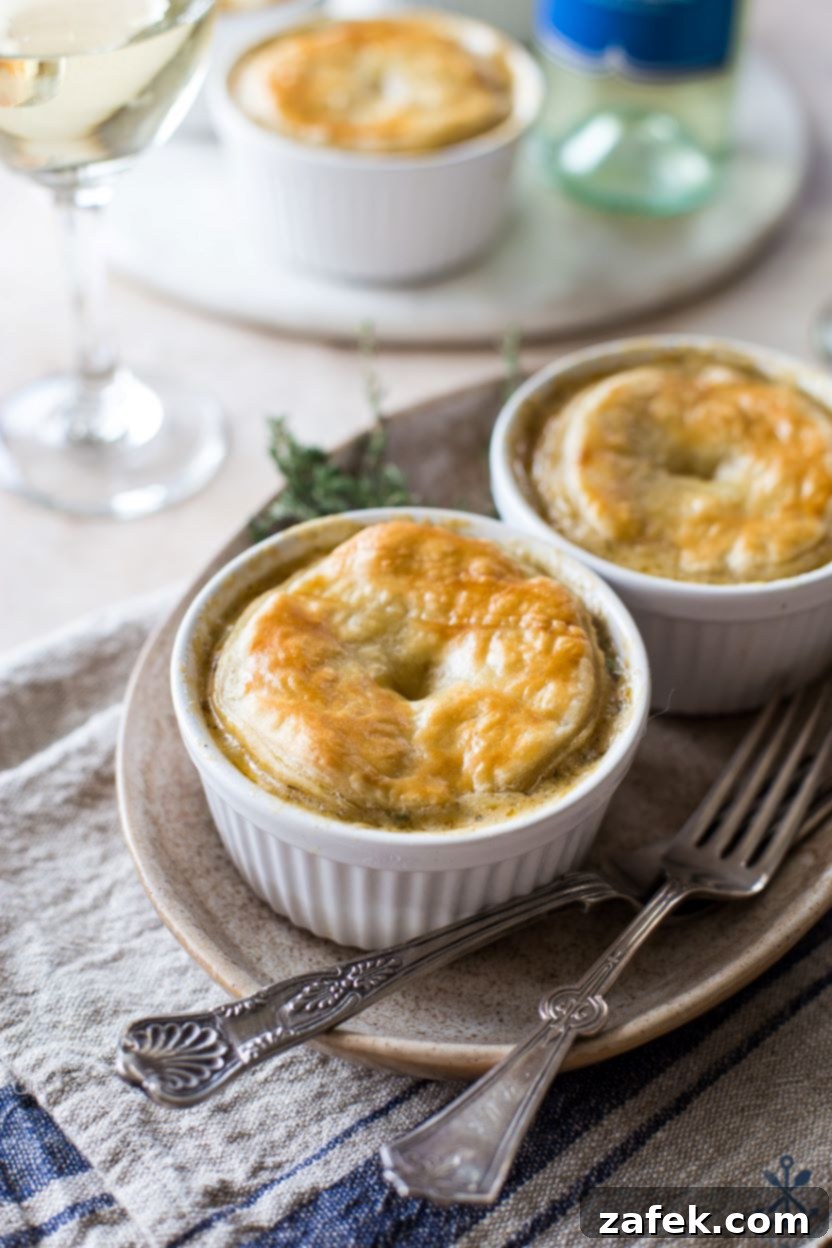 Flaky Puff Chicken Pot Pie 9 A close-up, inviting photograph of two individual Puff Pastry Topped Chicken Pot Pies, served on an oval plate with forks poised for tasting, highlighting the golden, flaky crust and rich filling.