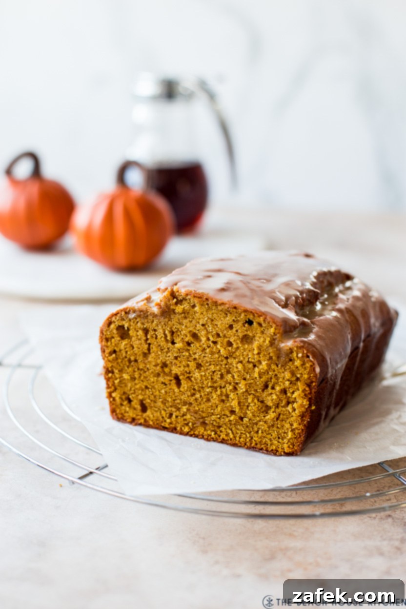 Cozy Maple Kissed Pumpkin Bread 3 A close-up shot of a glazed pumpkin bread loaf, showcasing the beautiful maple drizzle and its moist texture, placed on a wire cooling rack.