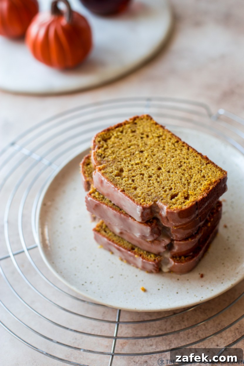 Cozy Maple Kissed Pumpkin Bread 5 A stack of golden brown, glazed pumpkin bread slices on a white plate, showcasing the fluffy interior.