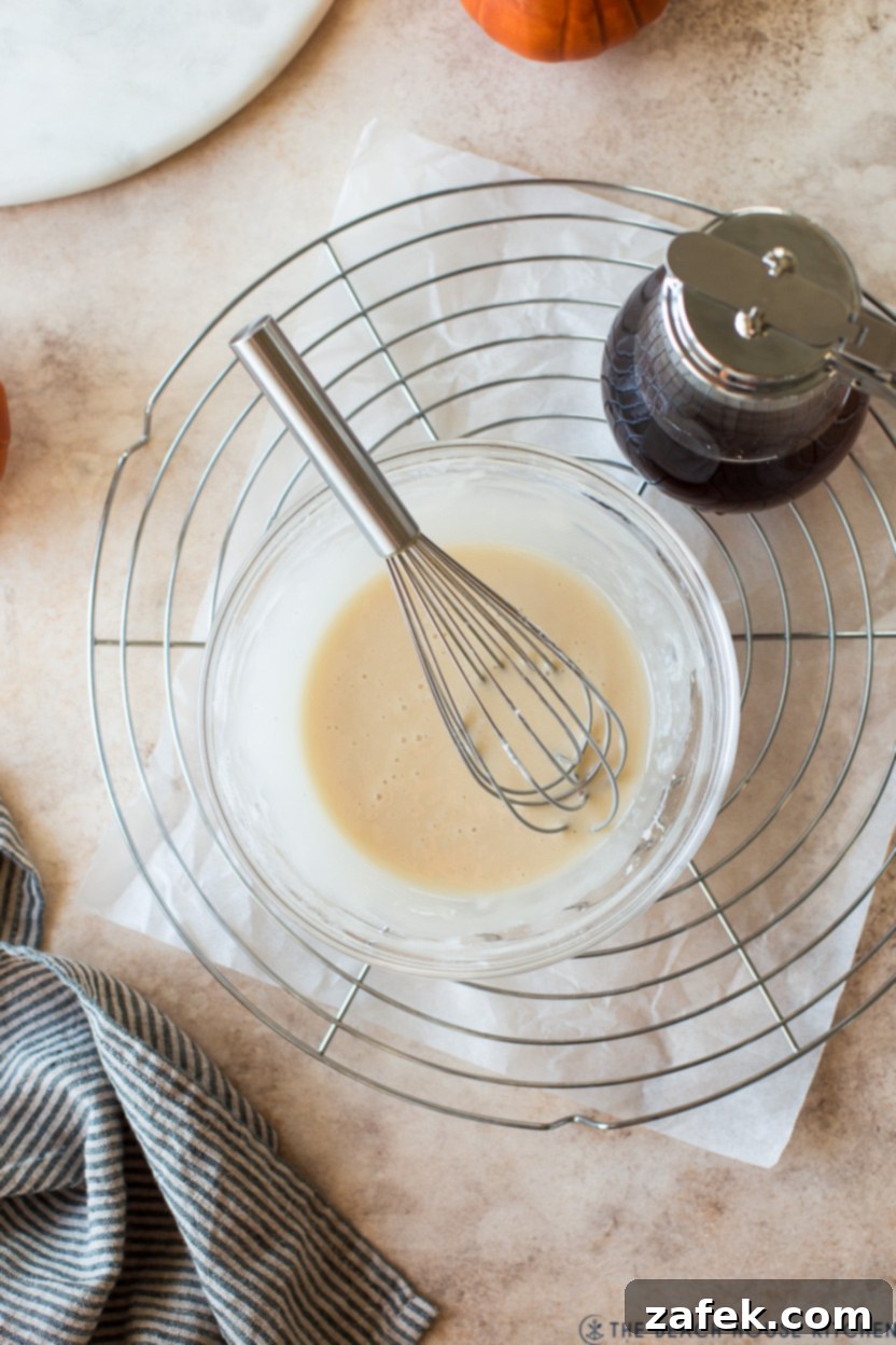Cozy Maple Kissed Pumpkin Bread 7 An overhead shot of a bowl of creamy maple glaze with a wire whisk, ready to be poured over the pumpkin bread.