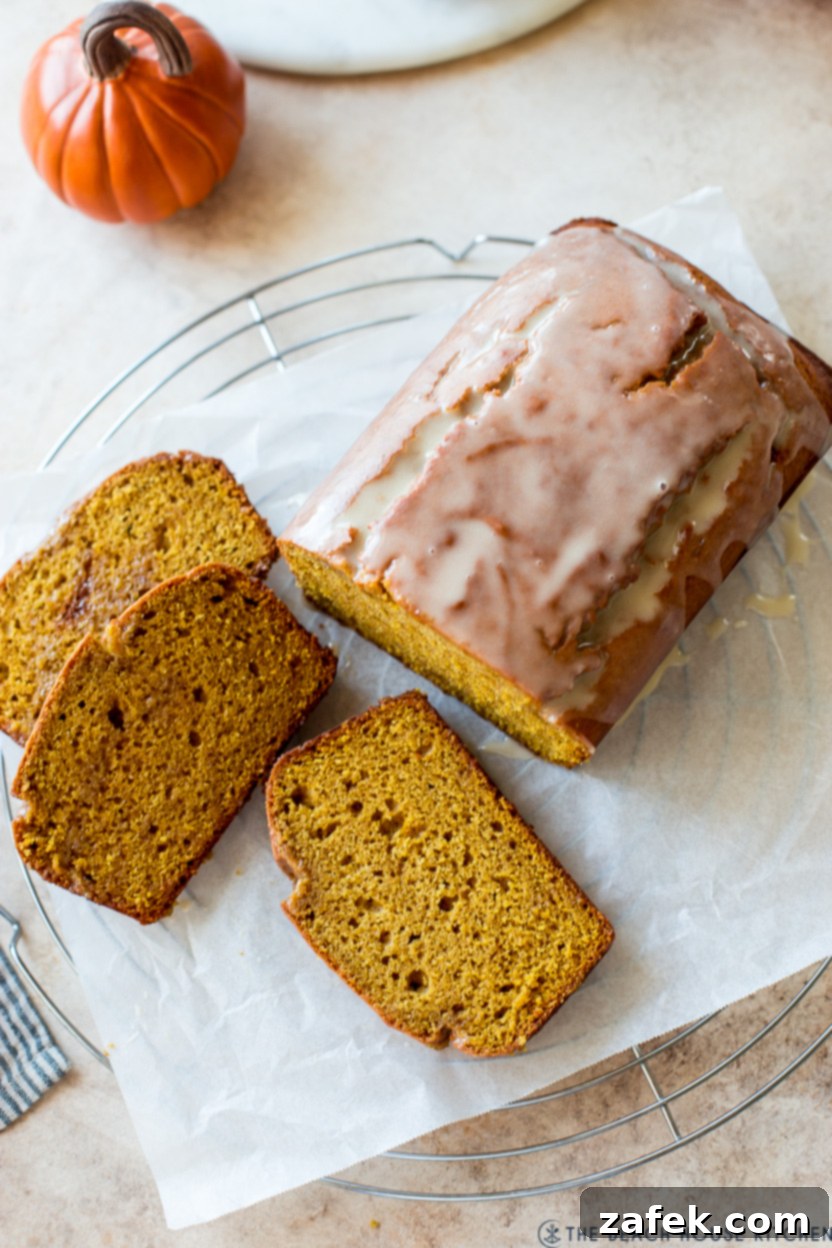 Cozy Maple Kissed Pumpkin Bread 8 A beautiful overhead view of a glazed pumpkin bread loaf with a few slices already cut, presented on a wire cooling rack.