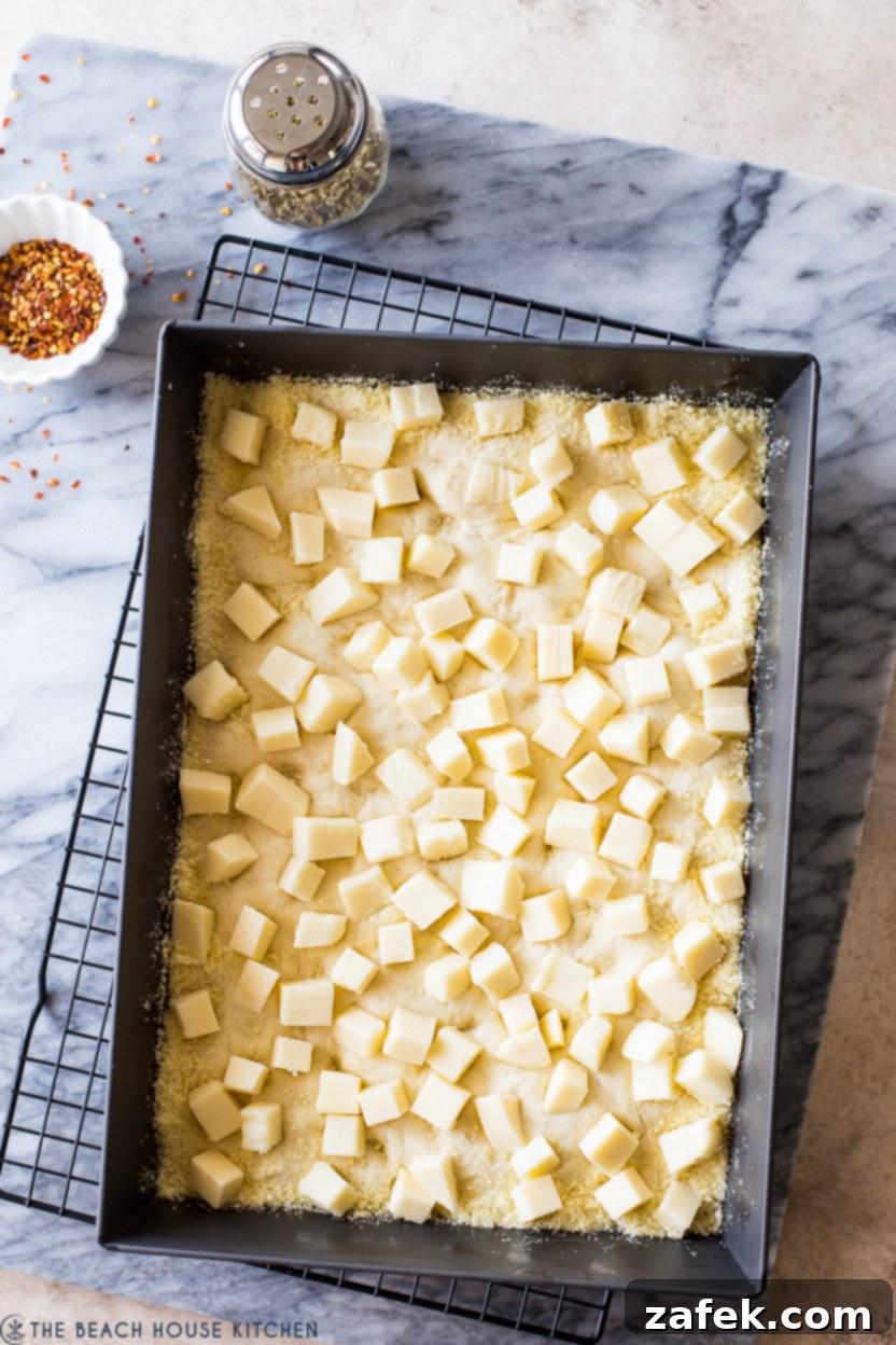 Overhead photo of a rectangular pan of pre-baked pizza dough topped with cubed cheese