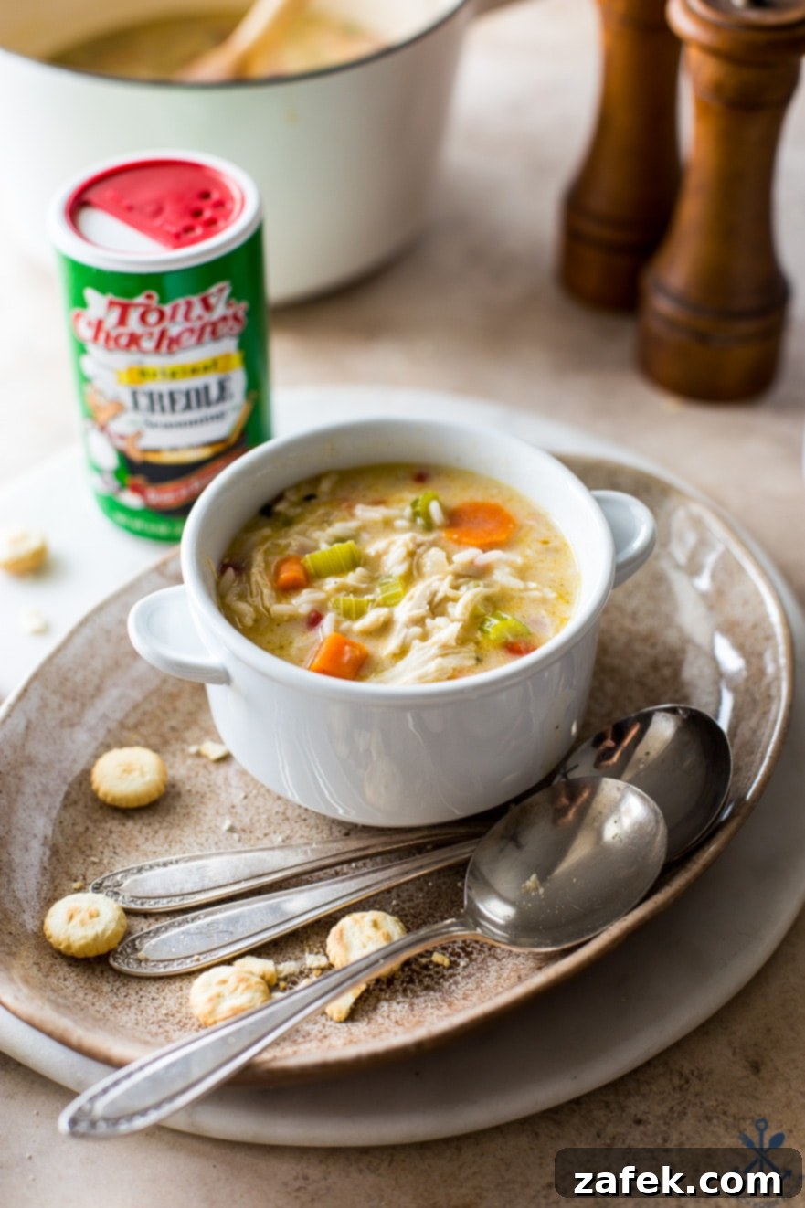 Soulful Cajun Chicken & Rice Soup 3 A vibrant bowl of Cajun Comfort Chicken and Rice Soup, adorned with a sprinkle of fresh herbs, served on an oval plate with accompanying spoons and crispy oyster crackers, inviting a cozy dining experience.