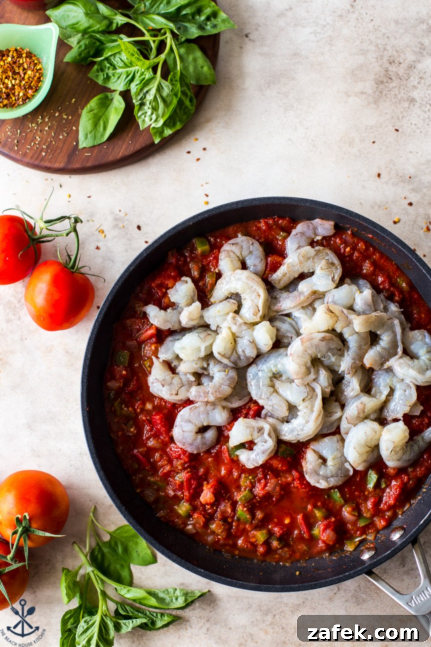 Greek-Style Baked Shrimp with Feta and Olives 7 Up close overhead photo of a skillet filled with a rich, red tomato mixture and raw shrimp nestled within, ready for baking