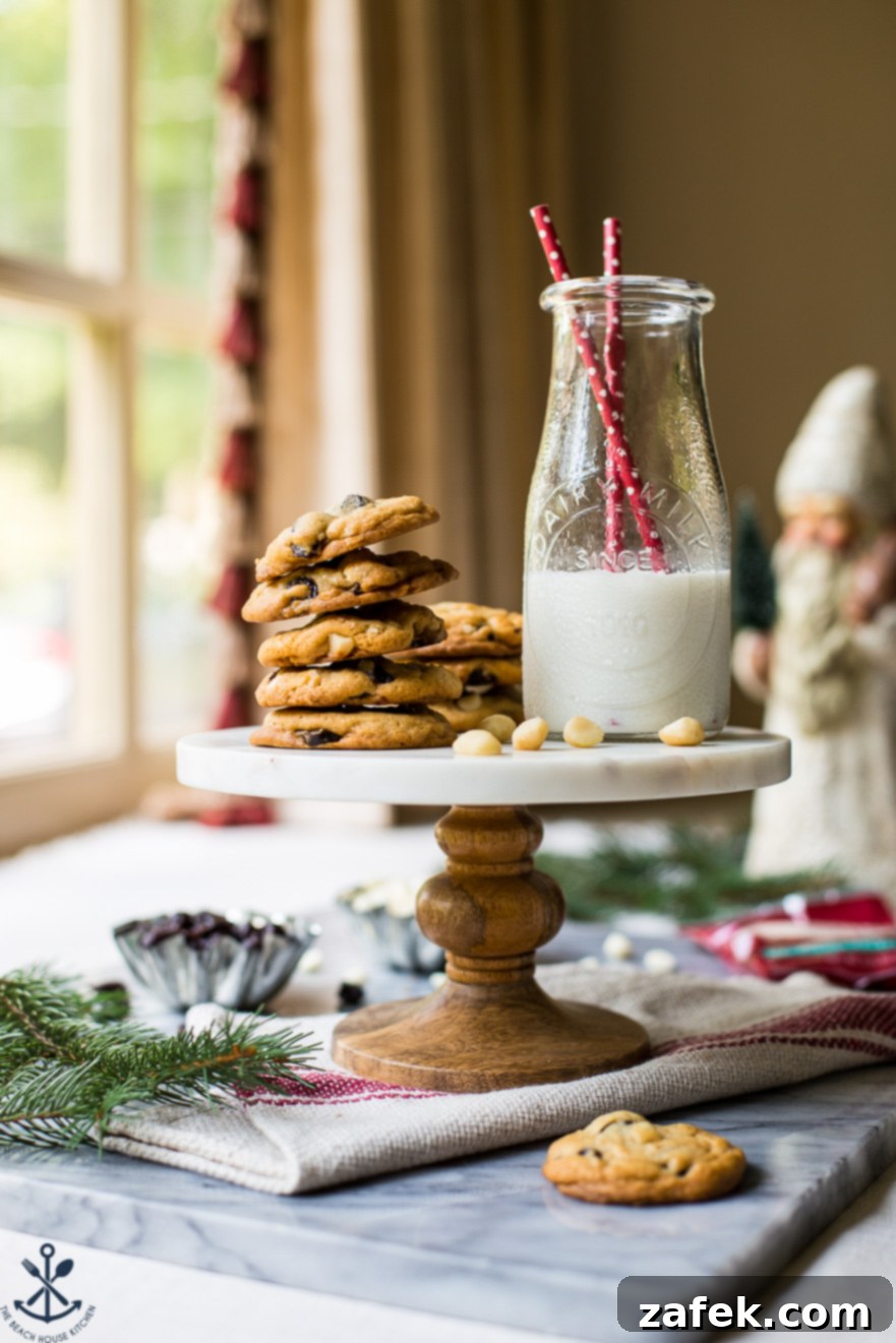 A cake stand topped with a stack of white chocolate cherry macadamia nut cookies and a bottle of milk with two red straws