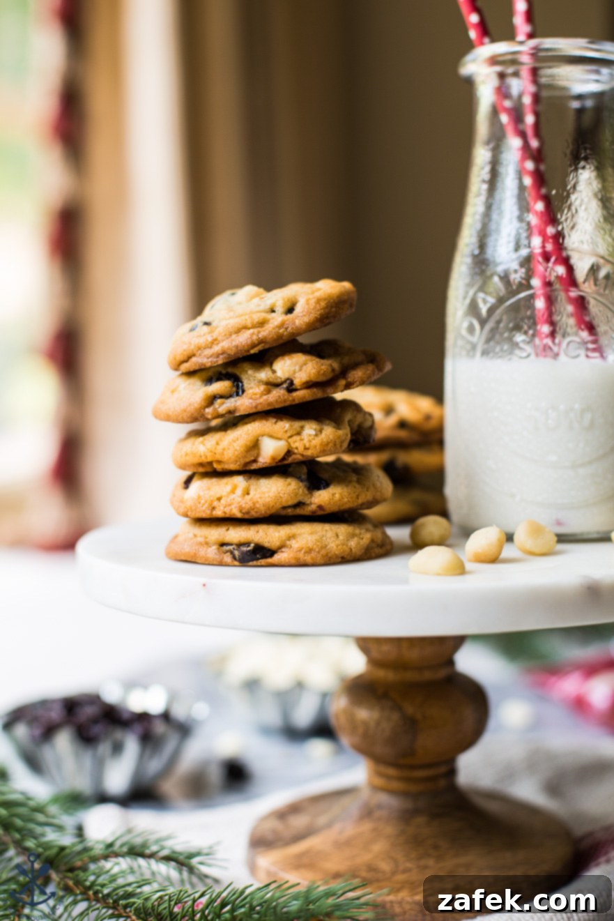 Up close photo of a cake stand topped with a stack of white chocolate cherry macadamia nut cookies and a bottle of milk with two red straws