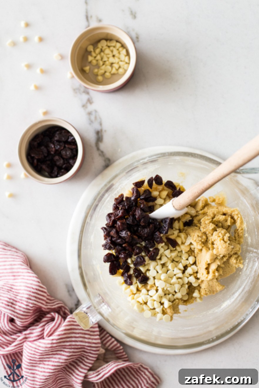 Overhead photo of a bowl filled with cookie dough, white chocolate chips and dried cherries with a small bowl of dried cherries and white chocolate chips off to the side
