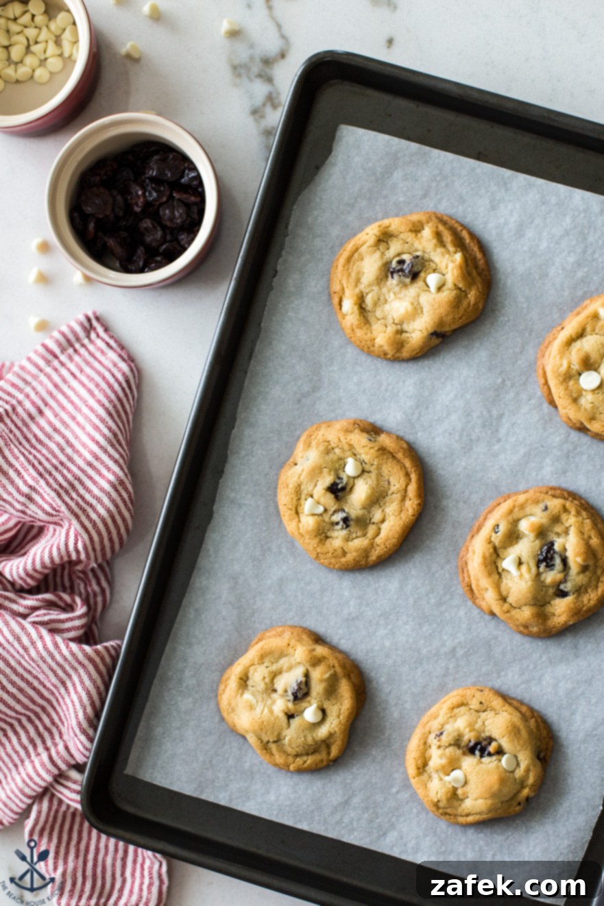 Overhead photo of a parchment-lined tray of cookies with a small bowl of dried cherries off to the side