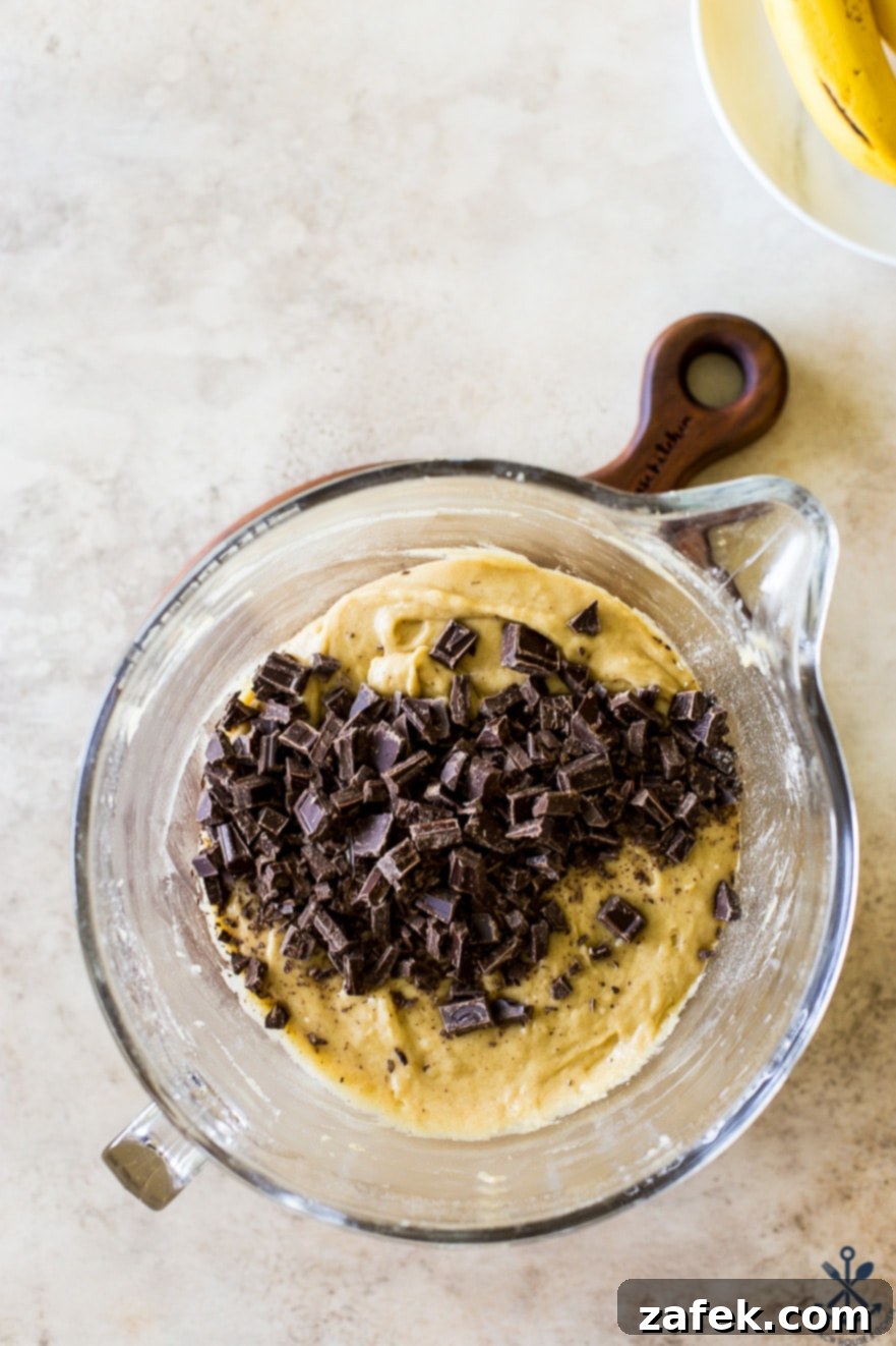 Decadent Bananas Foster Chocolate Chunk Cookies 5 Overhead view of a mixing bowl brimming with rich cookie batter, generously studded with bittersweet chocolate chunks, ready for baking