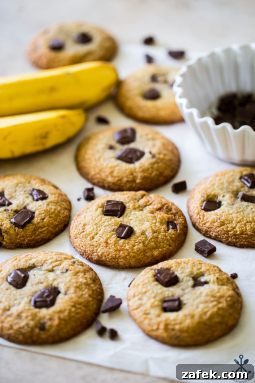 Decadent Bananas Foster Chocolate Chunk Cookies 6 A plate of freshly baked Bananas Foster Chocolate Chunk Cookies with ripe bananas and a bowl of chocolate chunks in the soft-focus background, inviting a delicious treat
