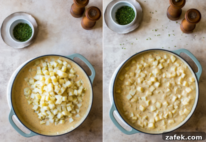 Cubed potatoes folded into a creamy, cheesy sauce in a cast iron skillet, ready for baking.