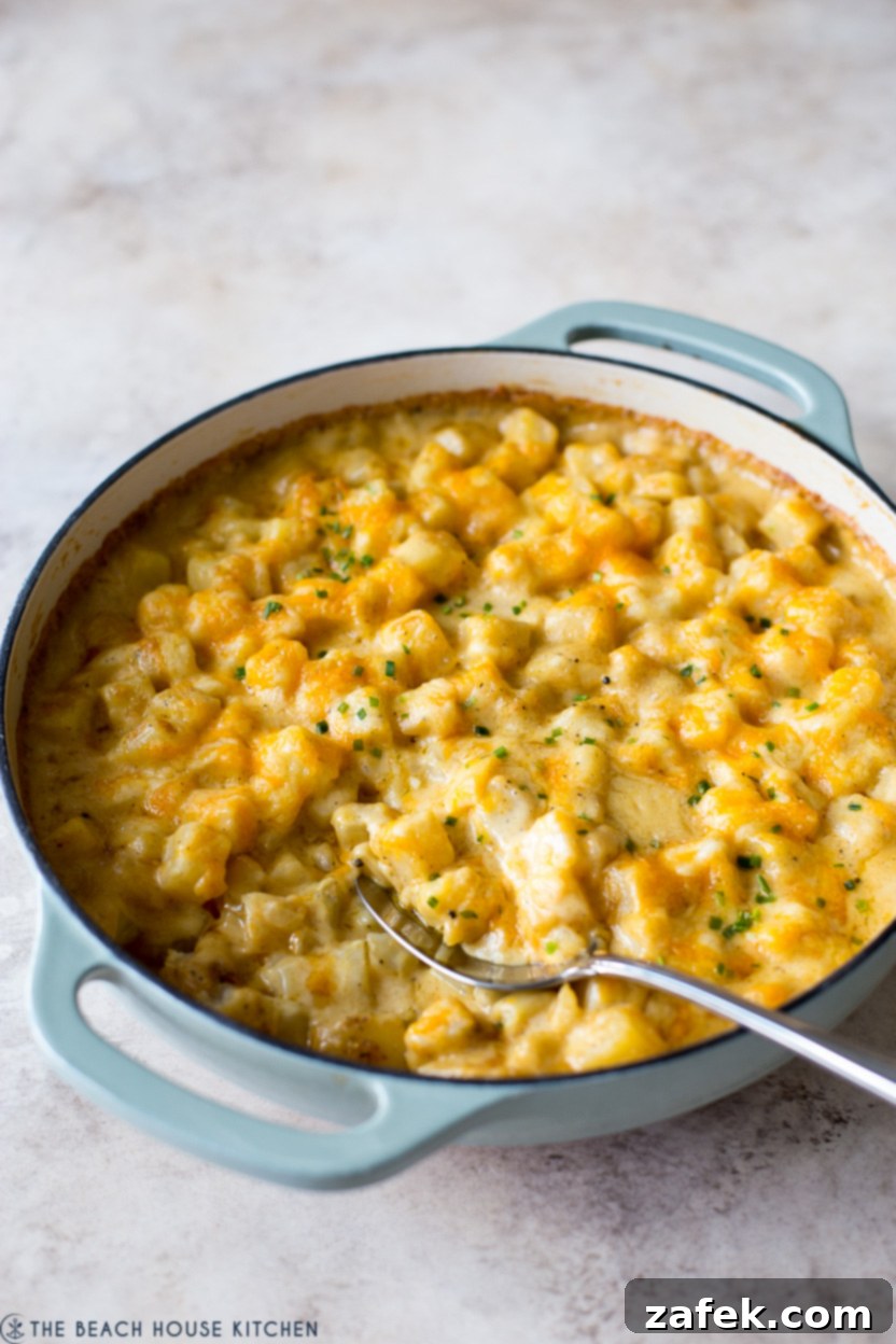 A cast iron skillet filled with golden-brown, bubbly cheesy potatoes, garnished with fresh green chives, ready to be served.