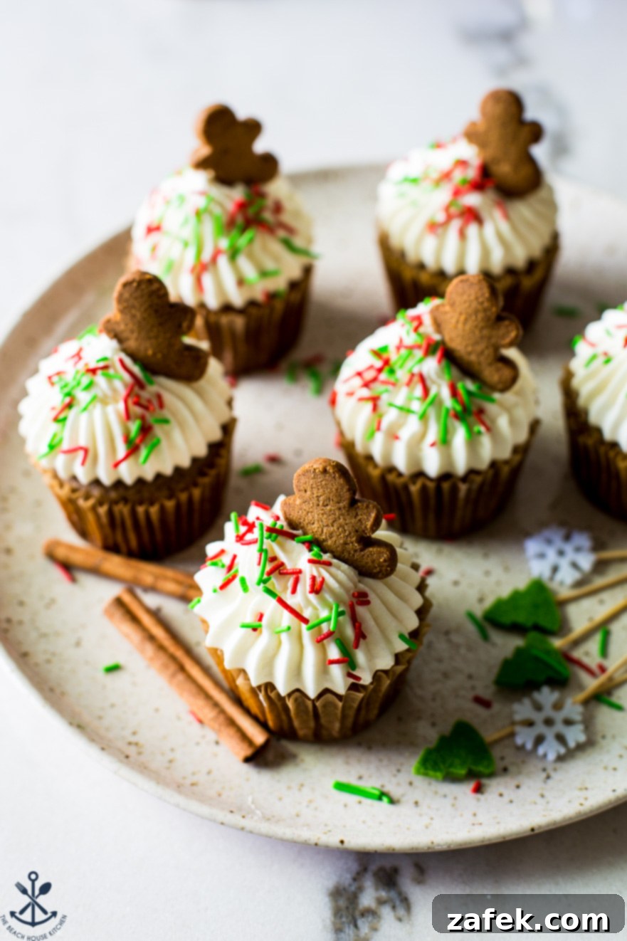 A plate of cream cheese frosted cupcakes with red and green sprinkles topped with a gingerbread man cookie