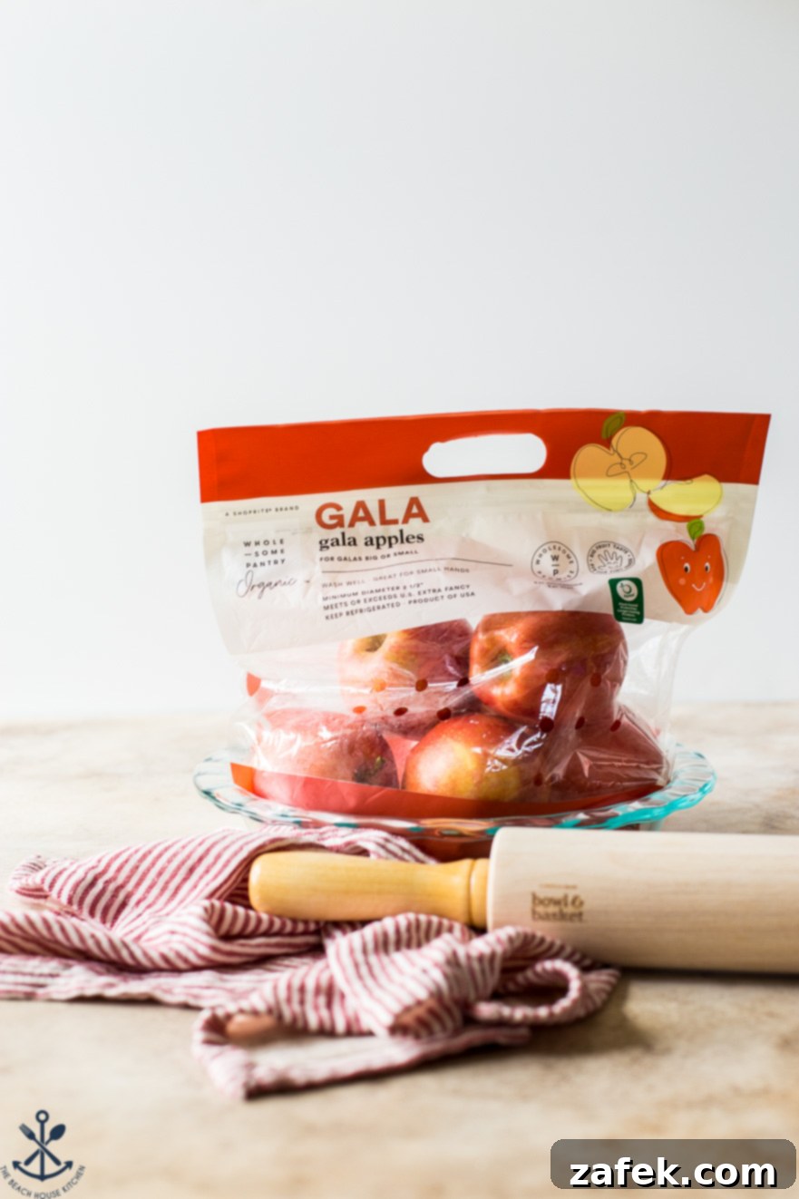 ShopRite's Holiday Apple Pie Fest 6 A clear plastic bag filled with crisp Gala apples next to a traditional wooden rolling pin, emphasizing fresh produce for apple pie.