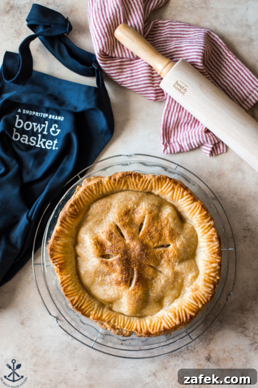 ShopRite's Holiday Apple Pie Fest 9 Overhead view of a baked apple pie, artfully arranged with a navy blue apron and wooden rolling pin on a rustic surface.