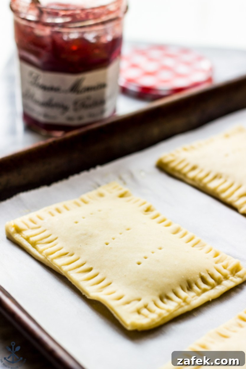 A pre-baked pop-tart on a parchment-lined baking sheet with a jar of jelly in the background