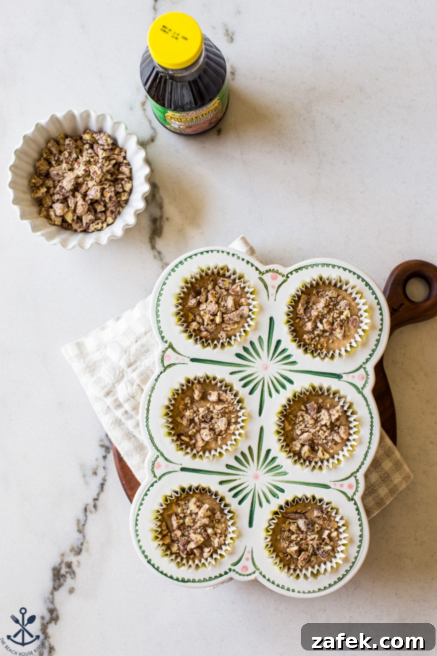 Golden Apple Praline Muffins 8 An overhead view of a muffin pan filled with unbaked Apple Praline Muffin batter, ready to go into the oven. A bowl of crunchy candied pecans sits nearby, along with a bottle of the distinctive praline honey ham marinade, setting the scene for a delicious baking session.