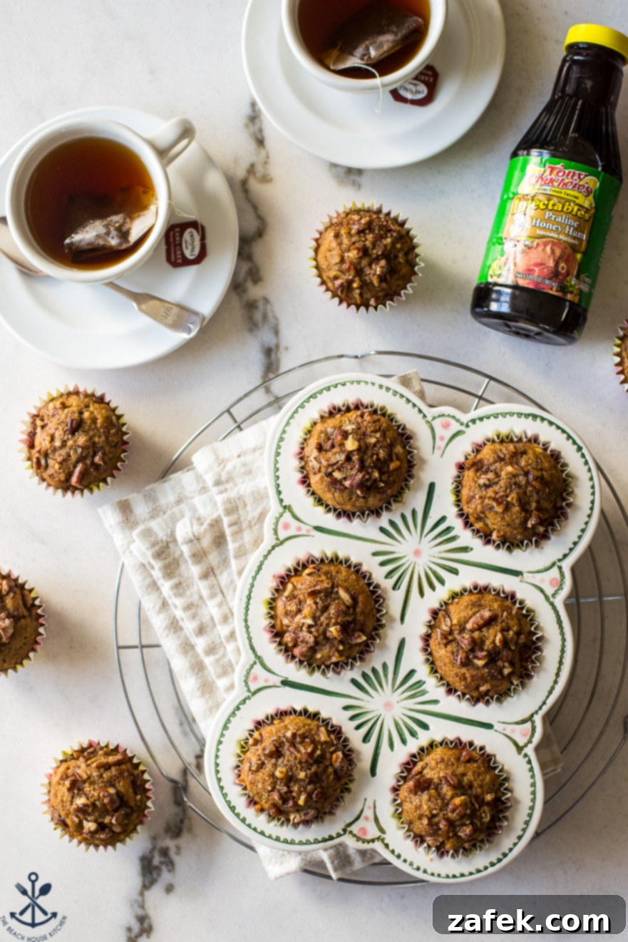 Golden Apple Praline Muffins 9 An inviting overhead photograph featuring a muffin pan filled with perfectly baked Apple Praline Muffins, positioned next to two cozy mugs, suggesting a warm and comforting breakfast scene. The muffins are golden and topped with pecans.