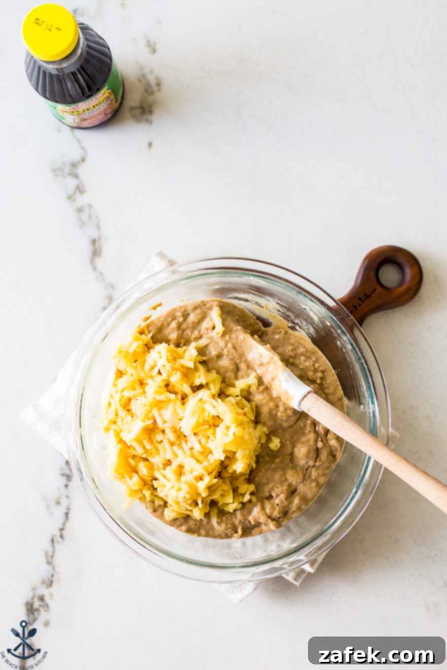 Golden Apple Praline Muffins 10 An intimate overhead shot of a mixing bowl containing a generous amount of Apple Praline Muffin batter, generously topped with freshly shredded apples, illustrating a key step in the preparation process before baking.