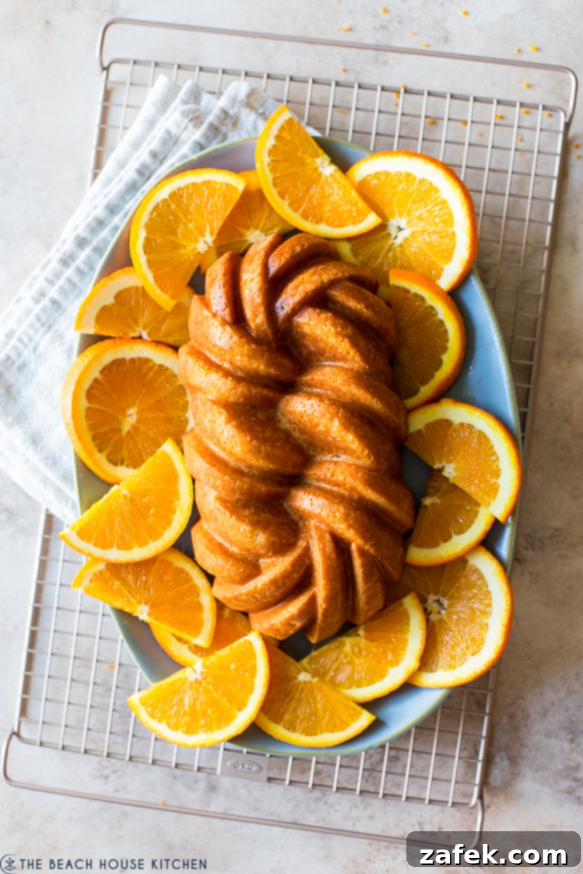 Overhead photo of an orange buttermilk loaf cake on a plate surrounded by orange slices