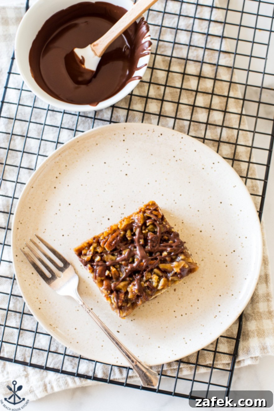 Decadent Maple Pecan Bars Adorned with Chocolate 2 Overhead photo of a perfectly sliced chocolate drizzled maple pecan bar on a plate with a fork, ready to be enjoyed