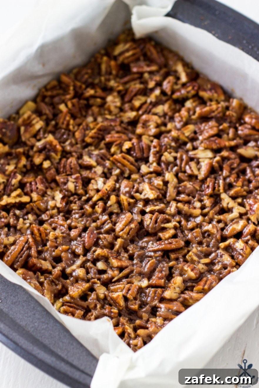 Decadent Maple Pecan Bars Adorned with Chocolate 7 Overhead photo of baked maple pecan bars in a 9x9 inch pan, showing the even distribution of the pecan topping before being cut and drizzled