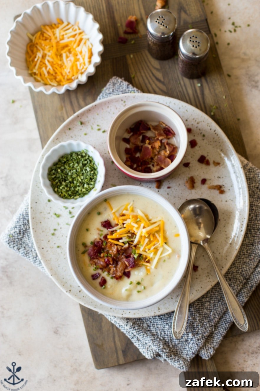 Bacon Cheddar Baked Potato Soup 4 Overhead photo of a bowl of soup topped with bacon and shredded cheese on a plate with a bowl of chives and a bowl of chopped bacon