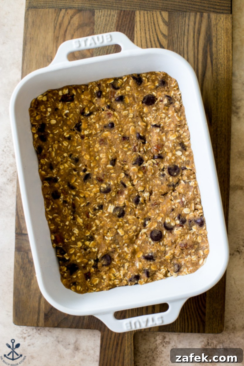 Chewy Oatmeal Chocolate Chip Bars 5 Overhead photo of unbaked oatmeal chocolate chip bar dough spread evenly in a pan on a wooden board