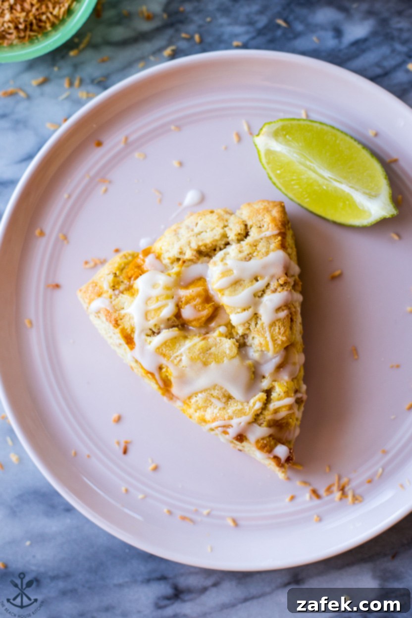 Up close overhead photo of a single lime glazed mango toasted coconut scone on a pink plate with a lime slice, highlighting its texture and glaze.