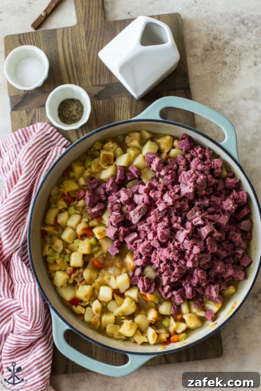 Overhead photo of a skillet showing cooked potatoes and vegetables, now combined with generous cubes of cooked corned beef.
