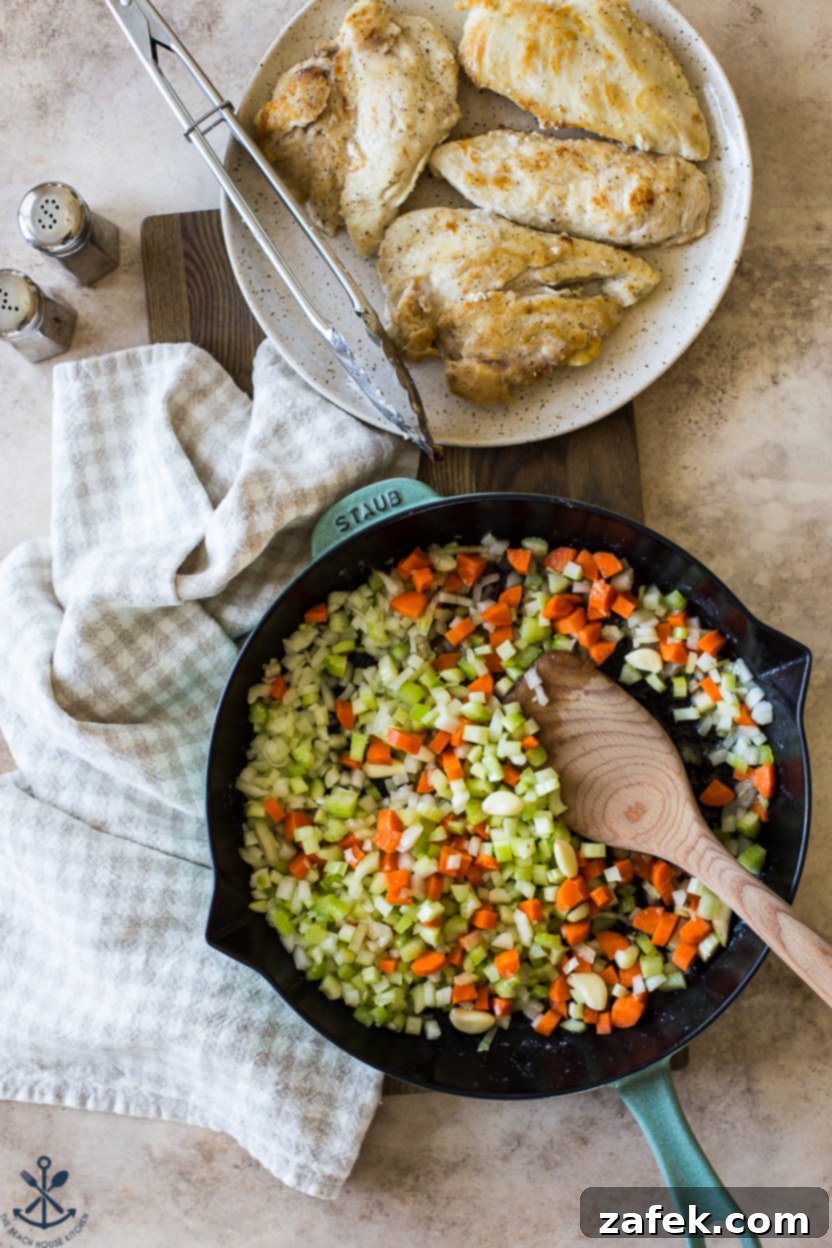 Garlic Chicken Delight 5 Overhead photo of a skillet filled with aromatic vegetables cooking, next to a plate of lightly browned chicken breasts