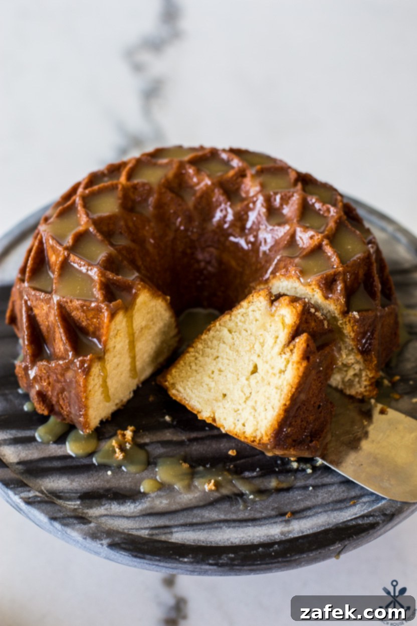Up close photo of a gloriously sliced brown sugar bundt cake, revealing its moist texture and topped with a generous amount of caramel glaze, served on a beautiful round cake pedestal.