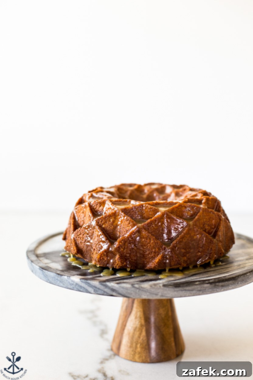 Up close photo of a glazed brown sugar bundt cake on a white cake pedestal, highlighting the shimmering caramel and the intricate cake texture, inviting a taste.