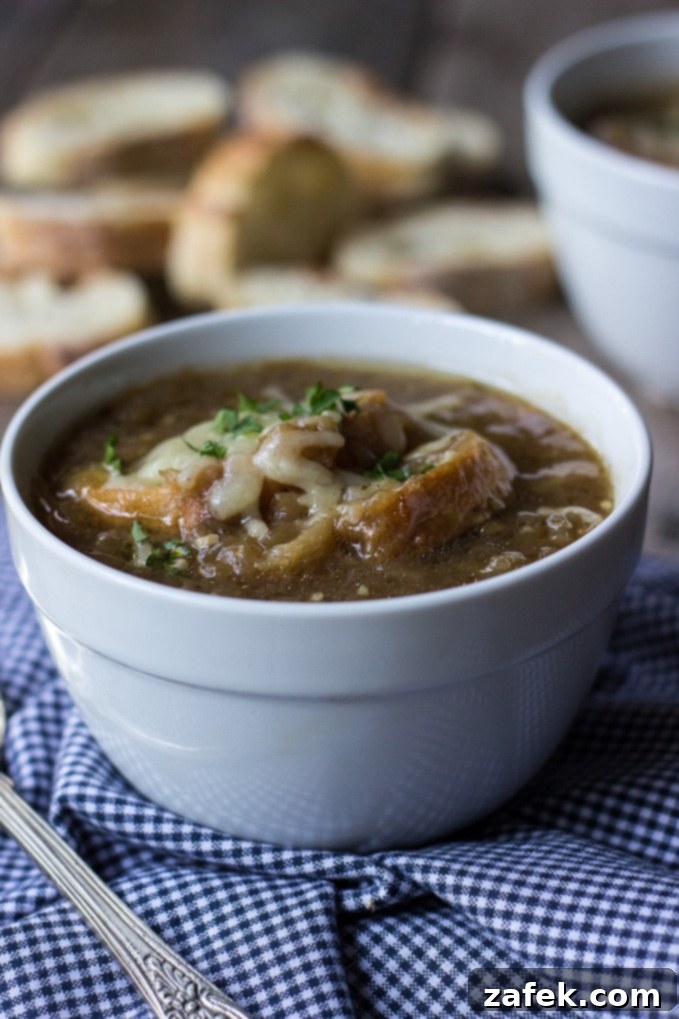 Rich Caramelized Onion Soup served in a white bowl with toasted baguette and shredded Gruyere cheese