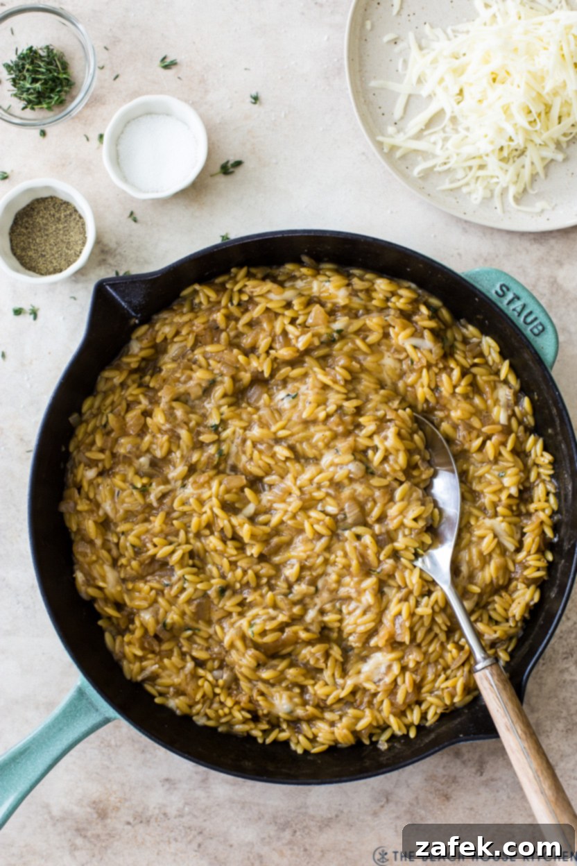 Overhead photo of a skillet of French Onion Orzo, garnished with fresh thyme and melted Gruyere cheese.