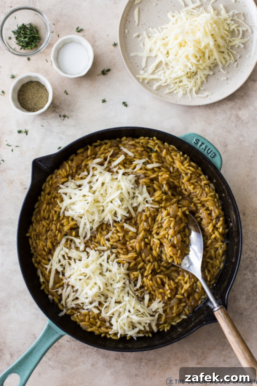 Overhead photo of a skillet of orzo topped with shredded gruyere cheese, melted and bubbling.