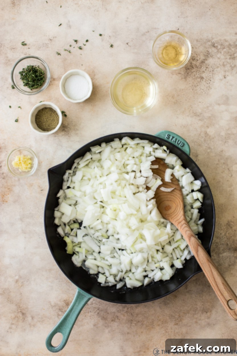 Overhead photo of a skillet of chopped onions with a few small bowls of spices, butter, and thyme.