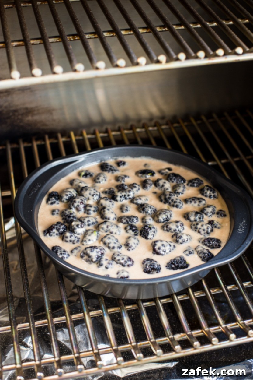 A baking pan fill with blackberries and biscuit batter on a grill